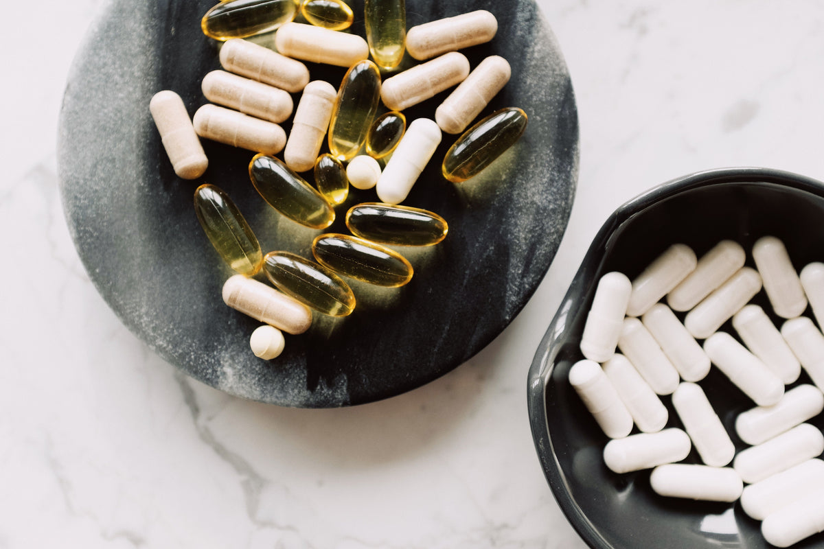 White supplement capsules and softgels in dark stone bowls on a marble table